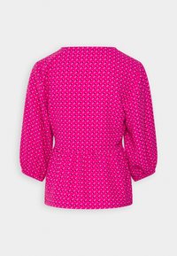 Blouse rose vif avec des manches trois-quarts bouffantes et un motif de petites formes diagonales blanches et noires.