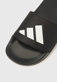 Sandalo nero a ciabatta con suola strutturata e tomaia liscia. Presenta tre strisce diagonali bianche sulla cinghia.