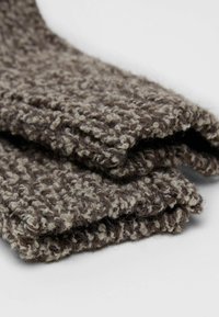 Sciarpa di lana lavorata a maglia marrone e beige con un motivo testurizzato. Il materiale appare spesso e caldo, con bordi pieghettati per dare struttura.