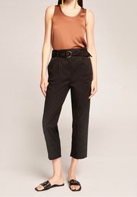 Brun satinlinne tillsammans med högmidjade svarta byxor med bältesmidja och en rund metallspänne. Svarta glidsandaler.