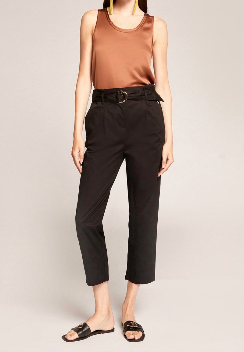 Brun satinlinne tillsammans med högmidjade svarta byxor med bältesmidja och en rund metallspänne. Svarta glidsandaler.