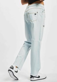 Lys blå denim jeans med avslappet passform, slitt kant og kontrasterende søm; kombinert med svarte og hvite sneakers.