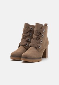 Bottes chelsea en suede marron avec un haut talon bloc, présentant un laçage frontal avec des lacets texturés et des accents décoratifs en métal argenté.
