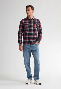 Rutete skjorte med knapper i marineblå, rød og grå; to brystlommer. Kombineret med lyseblå jeans og hvide sneakers. Glat tekstur.