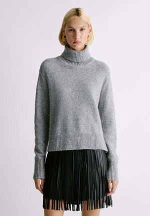 Maglione grigio a collo alto lavorato a maglia con polsini e orlo a coste, caratterizzato da accenti scintillanti. Abbinato a una gonna plissettata in ecopelle nera.