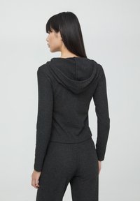 Felpa con cappuccio a maniche lunghe grigia scura, a coste, con un design aderente e una texture morbida. Presenta un cappuccio e maniche strette, vista da dietro.