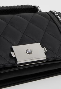 Petit sac en cuir matelassé noir avec fermoir rectangulaire argenté et bandoulière chaîne, mettant en valeur la texture et les détails métalliques brillants.