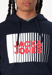 Felpa blu navy in cotone, con un design grafico a strisce verticali. Il logo "JACK & JONES" è in lettere rosse bold.