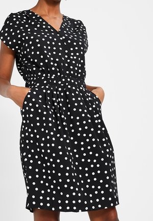Robe noire à pois blancs, col en V, manches courtes, taille élastique et poches, confectionnée en tissu léger.
