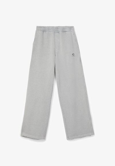 Pantalon gris clair à jambes larges avec taille élastique et poches latérales, comportant un petit logo noir sur la partie supérieure de la cuisse gauche.