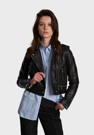 Black leather cropped jacket with zippered pockets, silver hardware, and a lapel collar, paired with a light blue button-up shirt.
