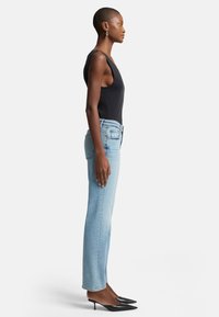 Top senza maniche nero, jeans dritti blu chiaro e décolleté neri a punta. Tessuto morbido, vestibilità su misura e design minimalista.