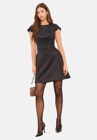 Čierne šaty s čiapkovými rukávmi a rozšírenou sukňou zo hladkej látky. Kombinované s nepriehľadnými pančuchami a lodičkami na opätku. Kabelka so zvieracím vzorom ako doplnok.