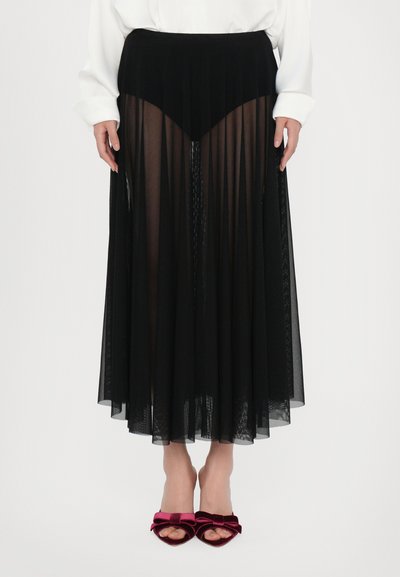 Falda larga negra y transparente con tejido texturizado, que presenta una cinturilla ajustada y una silueta fluida. Combinada con sandalias de tacón de terciopelo burdeos.