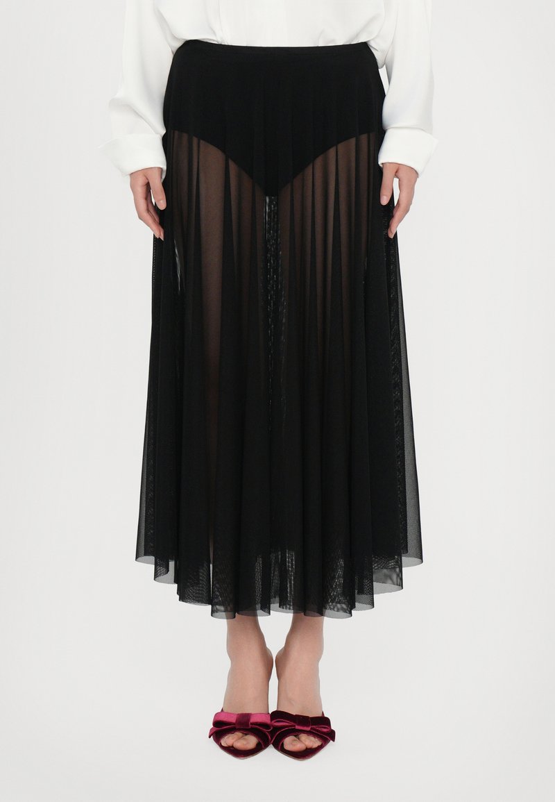 Falda larga negra y transparente con tejido texturizado, que presenta una cinturilla ajustada y una silueta fluida. Combinada con sandalias de tacón de terciopelo burdeos.