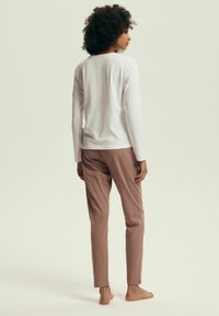 Biała bawełniana bluzka z długim rękawem i jasnobrązowe spodnie. Tkanina wydaje się miękka, z luźnym krojem i lekko zwężającymi się nogawkami.