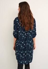 Marineblaues Kleid mit floralem Muster, lange Ärmel und aufgerollte Manschetten. Leichter Stoff, lockere Passform mit leicht gewelltem Saum.