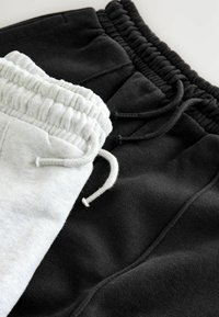 Zwei Paare vonSweatpants, eines in hellgrau und eines in schwarz, beide mit elastischen Taillenbünden und Kordeln. Weicher Fleece-Stoff.