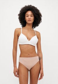 Hvit trekantet bralette med tynne stropper, kombinert med glatte, beige hipster-truser. Stoffet ser mykt og elastisk ut.