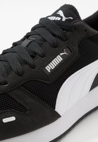 Adidași alb-negru cu un material texturat, realizat din plasă și suede, având șireturi negre și un logo Puma proeminent.