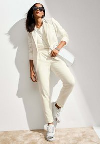 Witte op maat gemaakte pak met slim fit broek, gelaagd over een lichte top, gecombineerd met witte sneakers met zilveren accenten en een witte handtas.