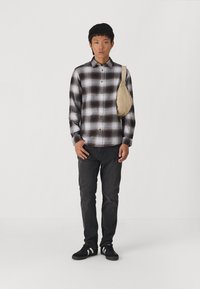 Rutet brunt og hvitt flanellskjorte, svarte skinny jeans, svarte sko med hvite striper og en beige crossbody veske.