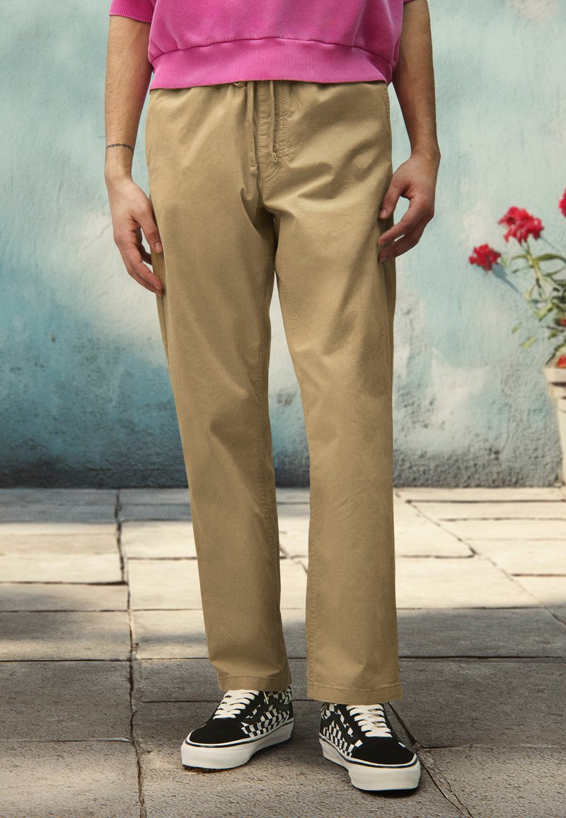 Beige, lette bomuldsbukser med lige pasform, parret med sorte sneakers med et hvidt og ternet mønster.
