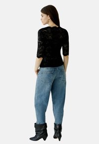 Schwarzes Spitzenoberteil mit Dreiviertelärmeln, kombiniert mit hellblauen, hochgeschnittenen Jeans. Das Modell trägt hohe, schwarze, lässige Stiefel.