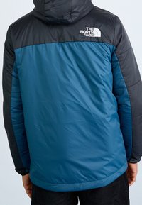 Puchowa kurtka z niebieską dolną częścią i czarną górną częścią. Posiada kaptur oraz biały logo "The North Face" na plecach.