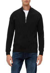 Schwarzer Zip-Hoodie aus geripptem Material mit Stehkragen und langen Ärmeln, kombiniert mit blauen Jeans.