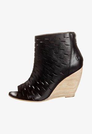 Bottine à talon compensé en cuir noir avec motif découpé, bout ouvert et talon en bois. Présente une fermeture éclair sur le côté pour un enfilage facile.