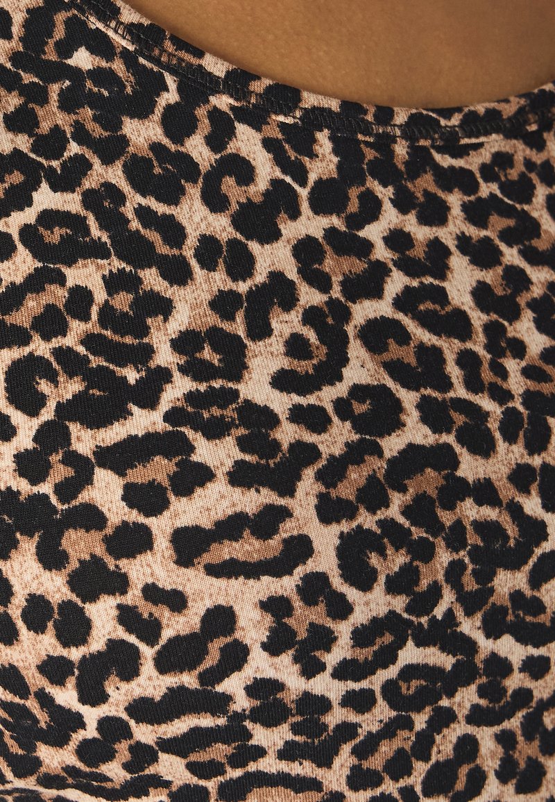 Leopardenmusterstoff mit einem sandbeigen Hintergrund und schwarzen Flecken, der eine gerippte Textur und einen weitem Halsausschnitt zeigt.