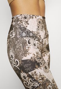 Legginsy z wysokim stanem, ozdobione kwiatowym i geometrycznym wzorem w odcieniach brązu i różu, wykonane z gładkiego, elastycznego materiału.