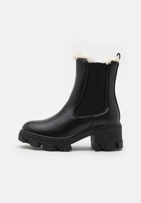 Botte de cheville en cuir noir avec un talon bloc épais, des panneaux élastiques sur les côtés et une bordure en fausse fourrure en haut. Semelle en caoutchouc texturé.