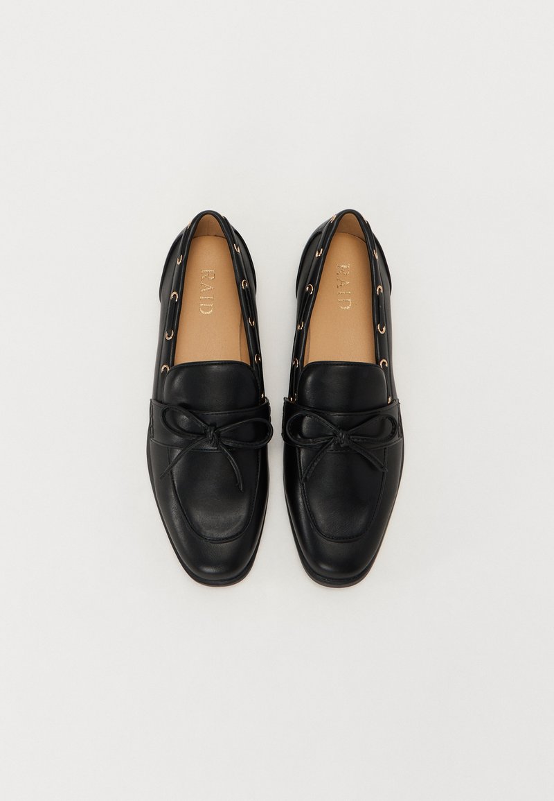Scarpe slip-on in pelle nera con forma arrotondata, decorate con un fiocco sul davanti e occhielli dorati sui lati.