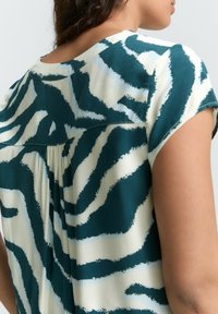 Blouse à manches courtes bleu canard et crème avec imprimé zèbre, dotée d'un détail de dos plissé et d'un col rond, confectionnée en tissu léger.