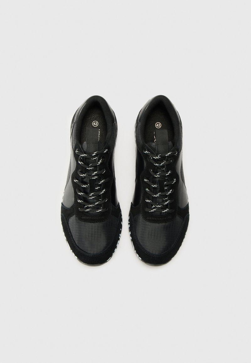 Zwarte sportieve schoenen met een textiel bovenwerk, contrasterende leren accenten, ronde veters en een rubberen zool met patroon. Maatlabel zichtbaar.