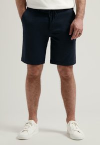 Marineblaue Shorts aus Baumwollmischung mit einem Kordelzugbund, seitlichen Taschen und geradem Schnitt. Kombiniert mit weißen Sneakers.