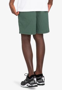 Pantaloni corti verdi con una vestibilità rilassata e orlo arrotolato, con dettagli di cucitura. Abbinati a scarpe da ginnastica nere e bianche.