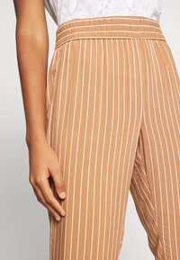 Pantalony s tan pruhy z lehké, měkké tkaniny. Mají elastický pas a svislé bílé pruhy pro elegantní vzhled.