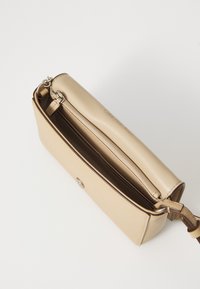 Borsa in pelle beige con texture liscia, chiusura con zip e dettaglio in metallo a forma di chiave. Tasca interna visibile, che mostra una fodera morbida.