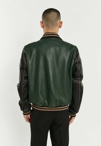 Veste bomber en cuir vert avec manches en cuir noir, col et taille côtelés, présentant des coutures contrastantes et une texture lisse.