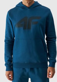 Sudadera ligera en color teal con logo negro, con bolsillo tipo canguro, puños y bajo acanalados, hecha de una suave mezcla de algodón.