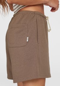 Braune Baumwollshorts mit einem Kordelzugbund, Seitentasche und einem Etikett auf der Rückseite. Weiche Textur mit lässigem Design.