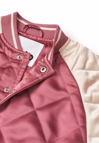 Giubbotto bomber imbottito con design trapuntato in rosa tenue, con dettagli in crema e colletto a righe. Dettaglio di chiusura a scatto visibile.