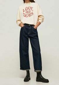 Felpa color avorio con stampa "LOVE AND JEANS", abbinata a jeans a gamba larga blu scuro e stivaletti neri con suola spessa.