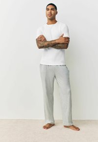 White short-sleeve shirt with a ribbed texture, paired with light grey sweatpants. Both have a relaxed fit and soft fabric.
