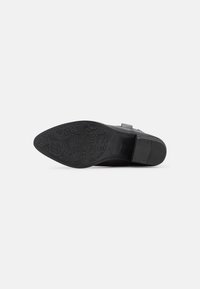 Suela de zapato negra con un patrón floral texturizado y un tacón liso; presenta una lengüeta elevada y un perfil plano para mayor estabilidad.