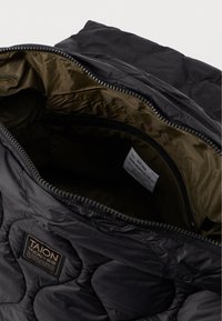 Μαύρη καπιτονέ τσάντα με φερμουάρ με λεία υφή και αντίθετη ελαιόχρωμη εσωτερική επένδυση; διαθέτει ετικέτα και μικρή τσέπη με φερμουάρ στο εσωτερικό.