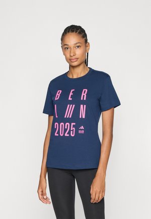 Navy blue cotton T-shirt featuring bold pink text "BERLIN 2025" and Adidas logo printed on the front. Short sleeves and crew neck design.
